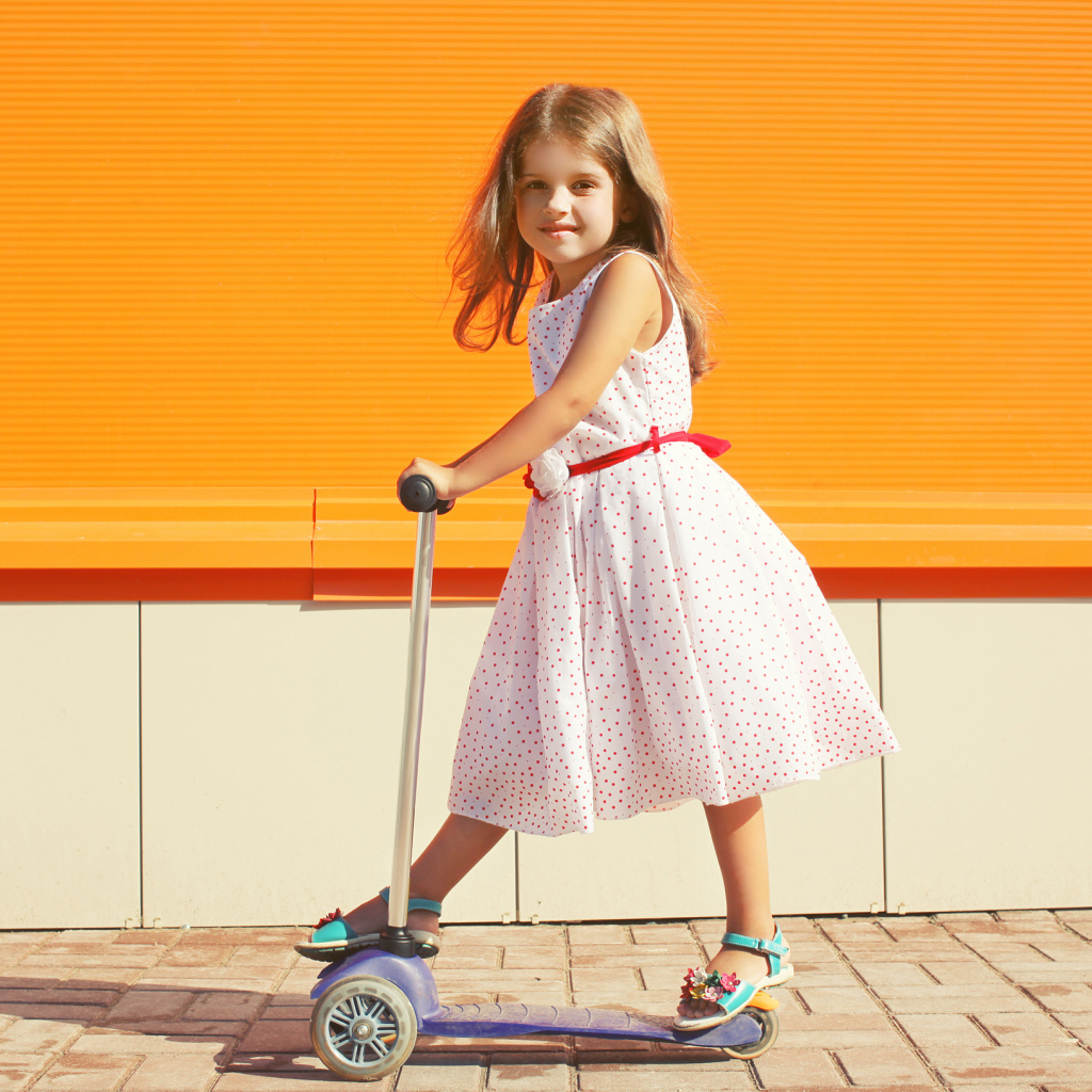 Маленькая девочка в платье на самокате 
