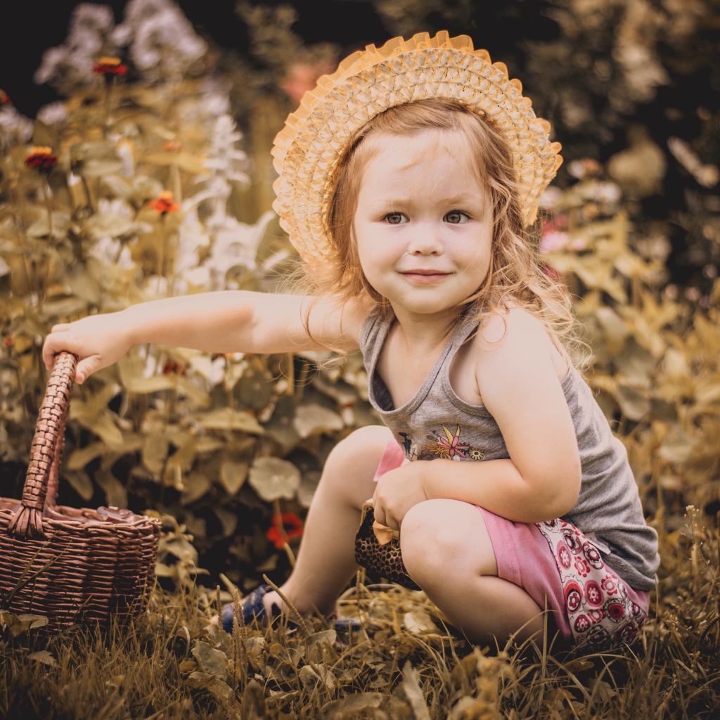 Маленькая девочка в шляпе сидит на траве с корзиной