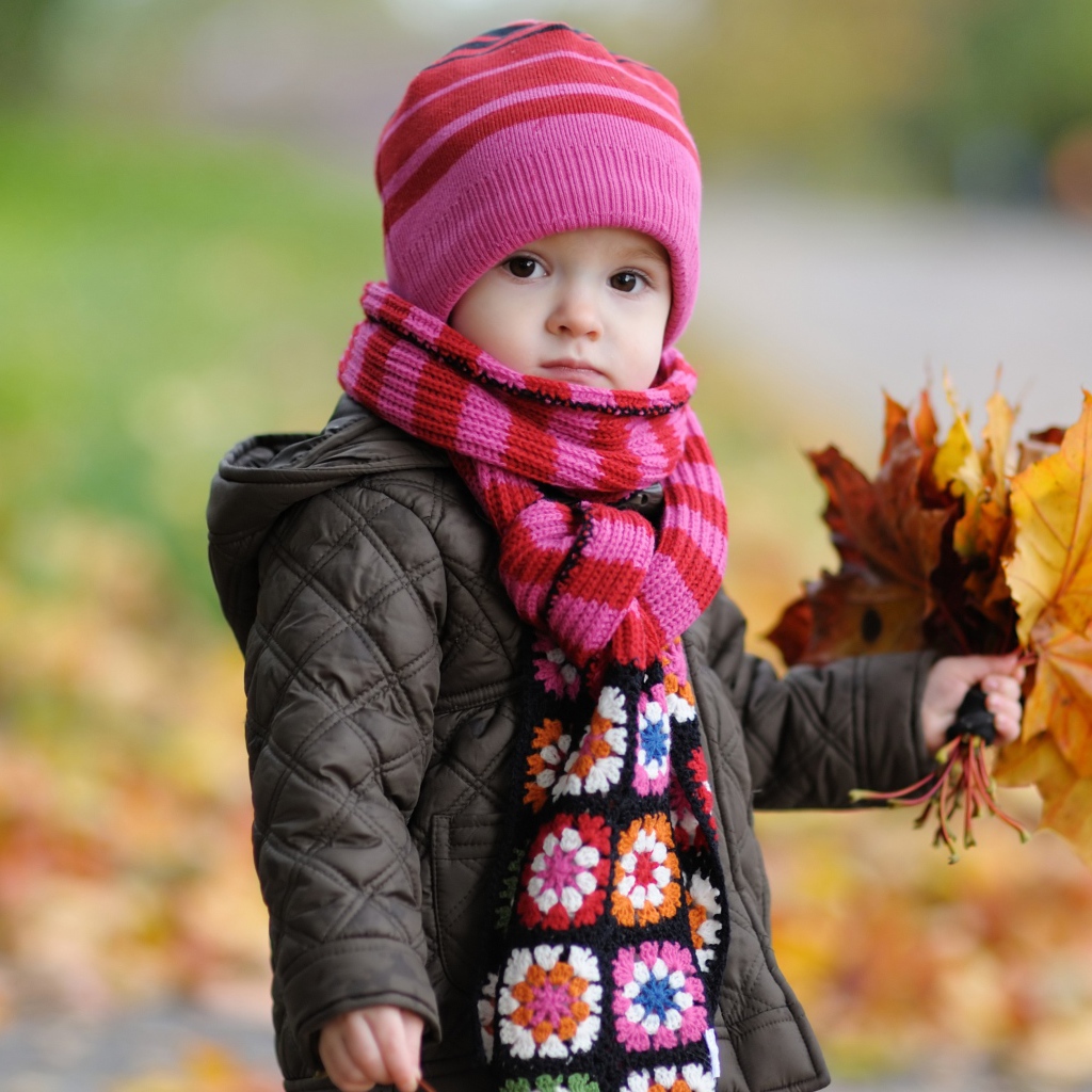 Маленькая девочка в розовой шапке с листьями в руке