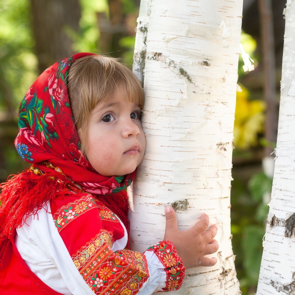 Маленькая девочка в красном платке обнимает березу