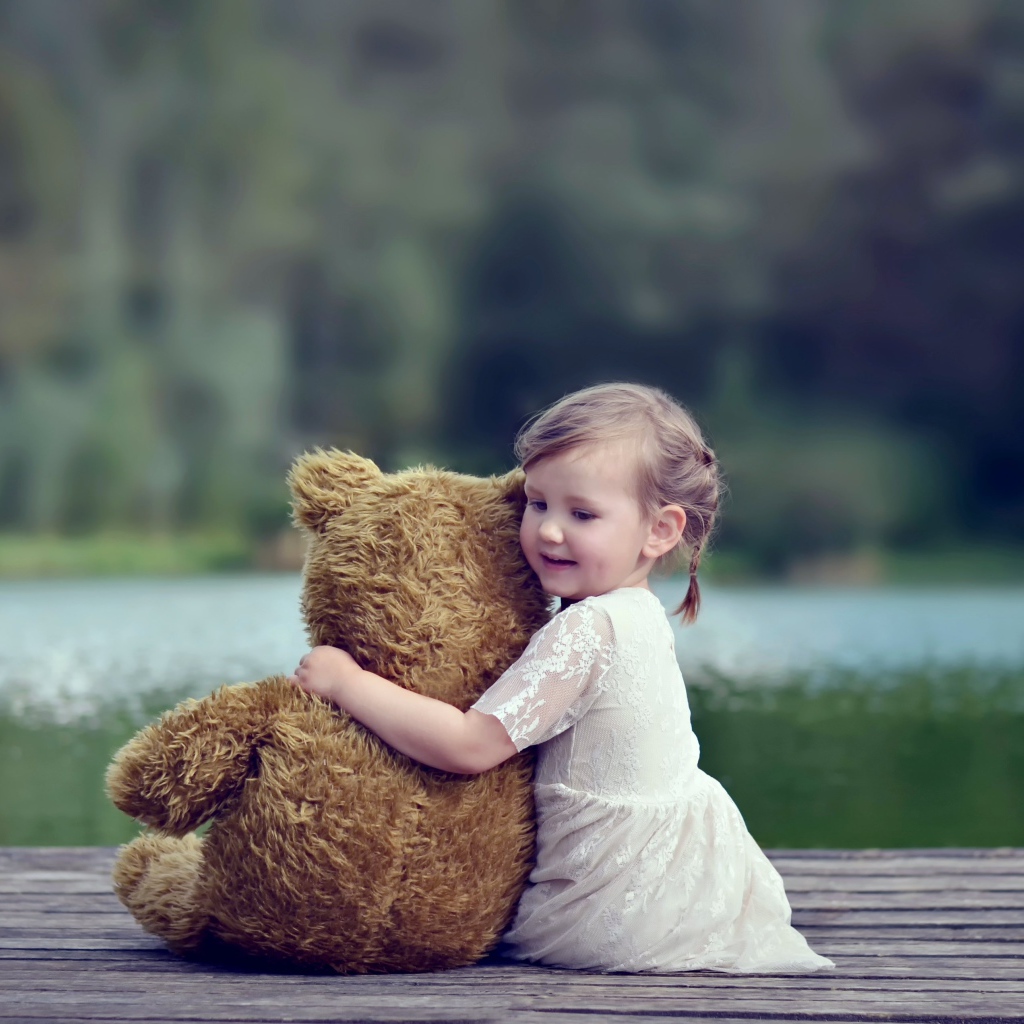 Маленькая девочка в белом платье сидит на мосту с плюшевым медведем