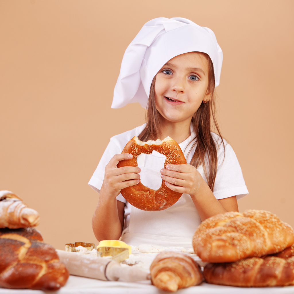 Маленькая девочка в костюме повара и свежей выпечкой