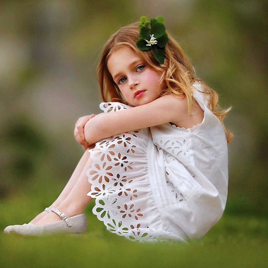 Маленькая девочка в белом платье сидит на зеленой траве