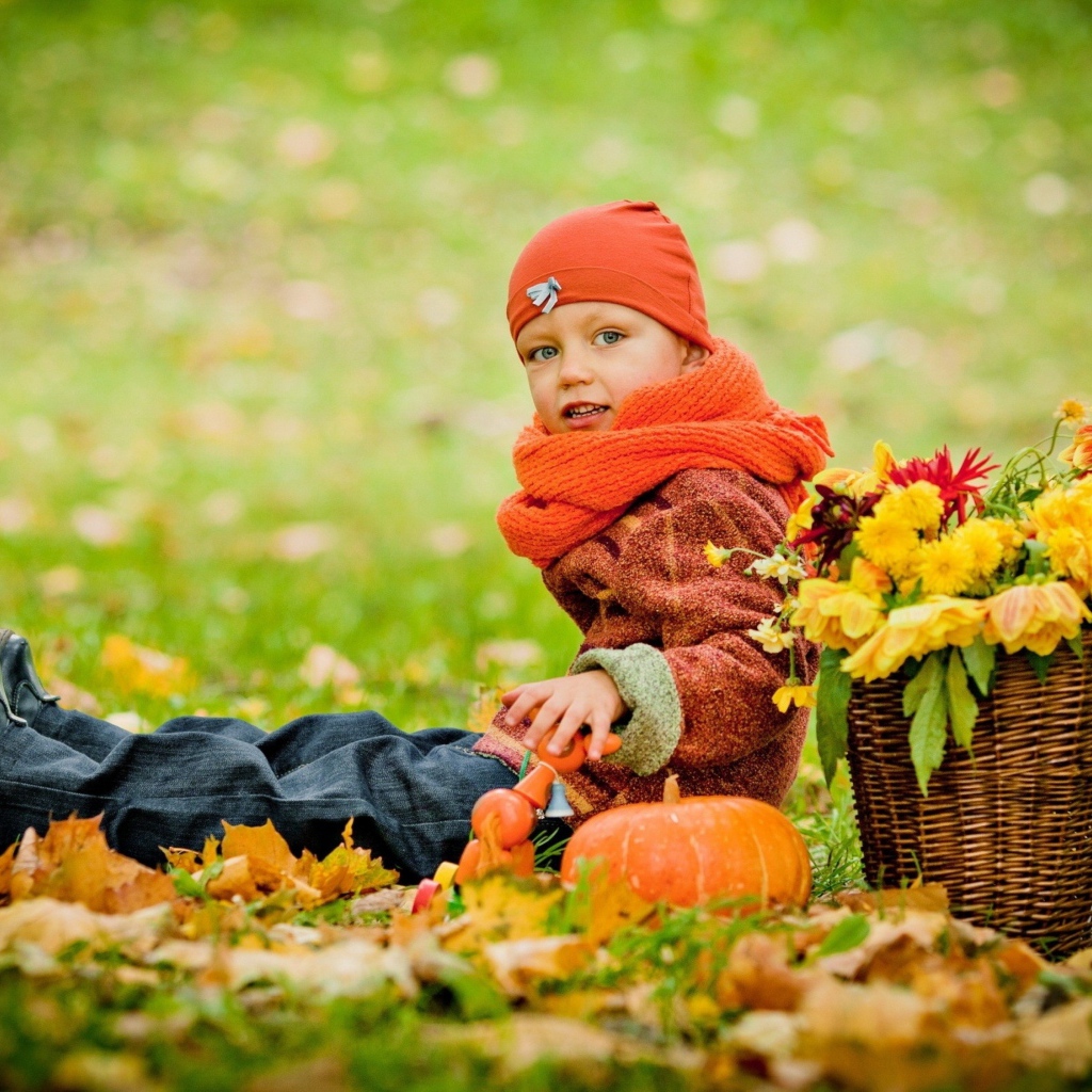 Маленькая девочка сидит на траве с корзиной цветов осенью