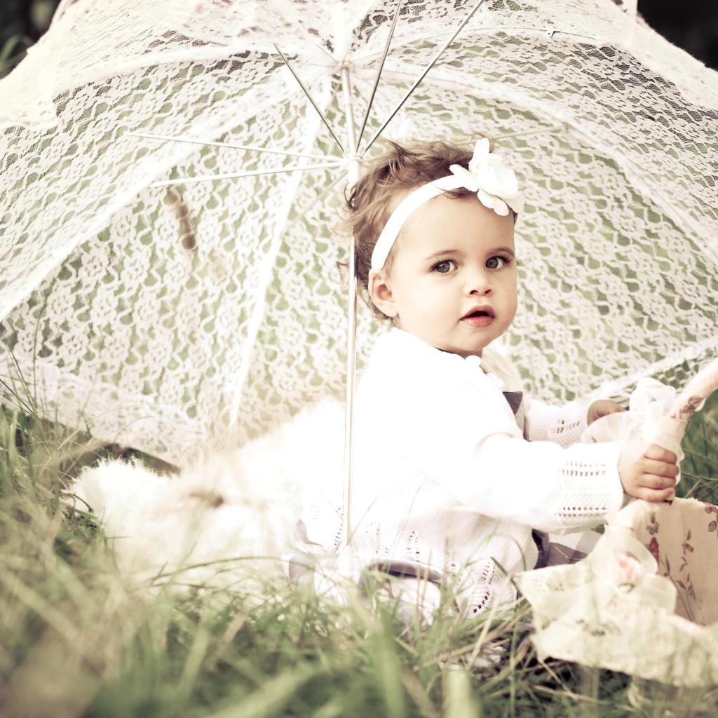 Маленькая девочка сидит на траве с большим белым зонтом