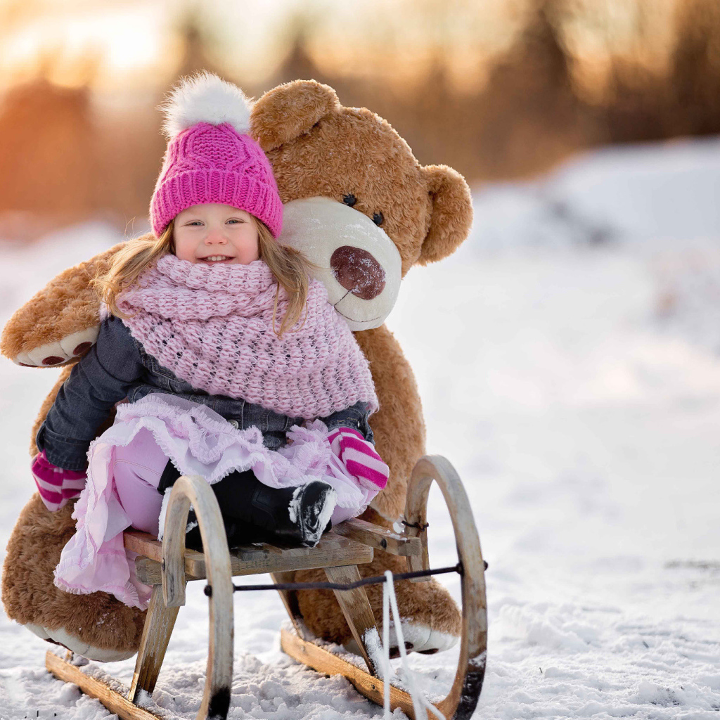 Маленькая девочка на санках с большим медведем зимой 