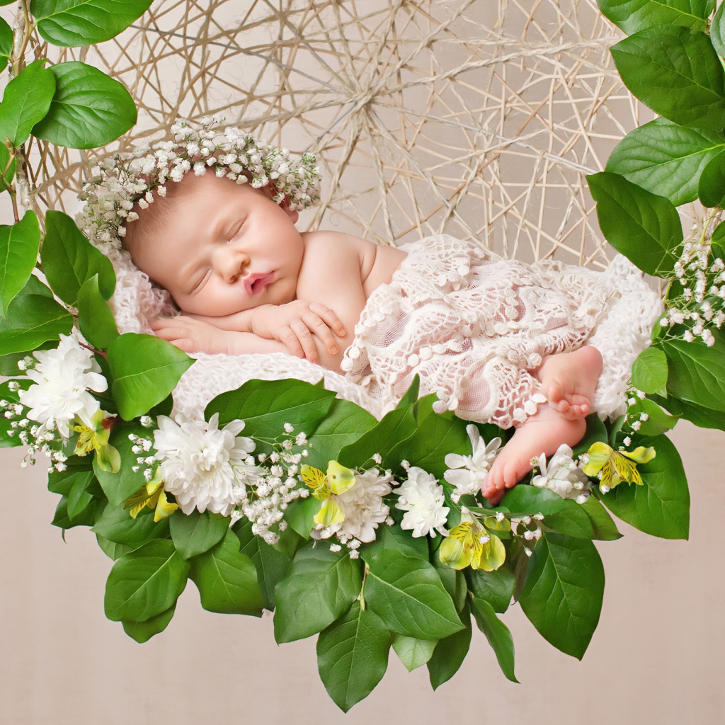 Маленькая девочка спит в колыбеле украшенной зелеными листьями