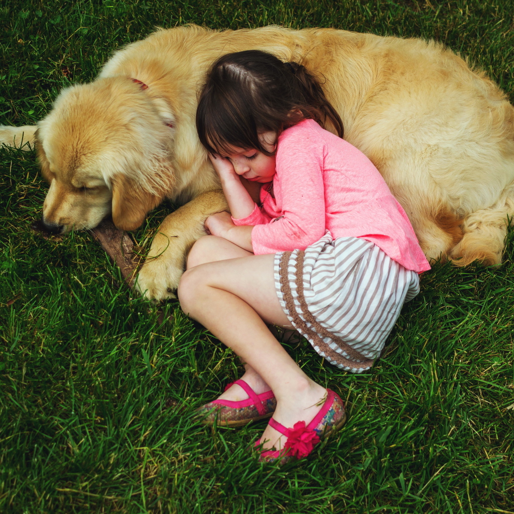 Маленькая девочка спит на зеленой траве с собакой