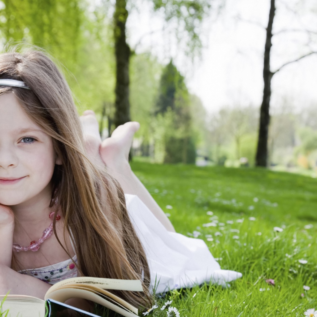 Маленькая девочка с книгой лежит на зеленой траве