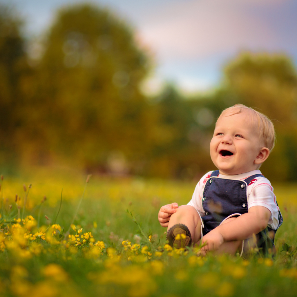 Маленький смеющийся мальчик сидит на траве с желтыми цветами