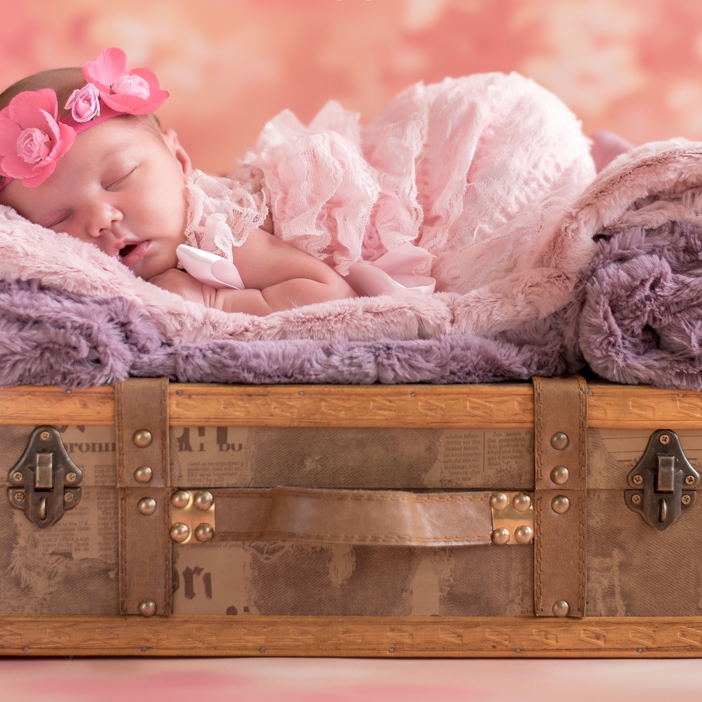 Маленькая новорожденная девочка спит на чемодане