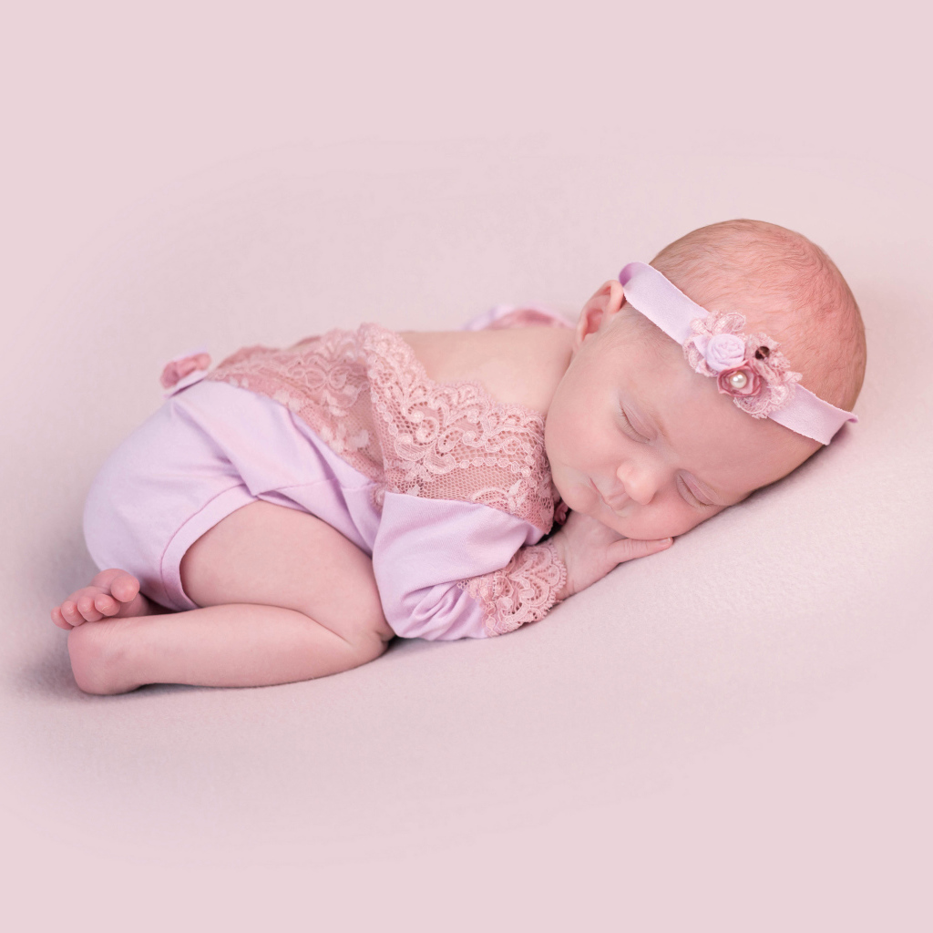 Маленькая новорожденная девочка с повязкой на голове на розовом фоне