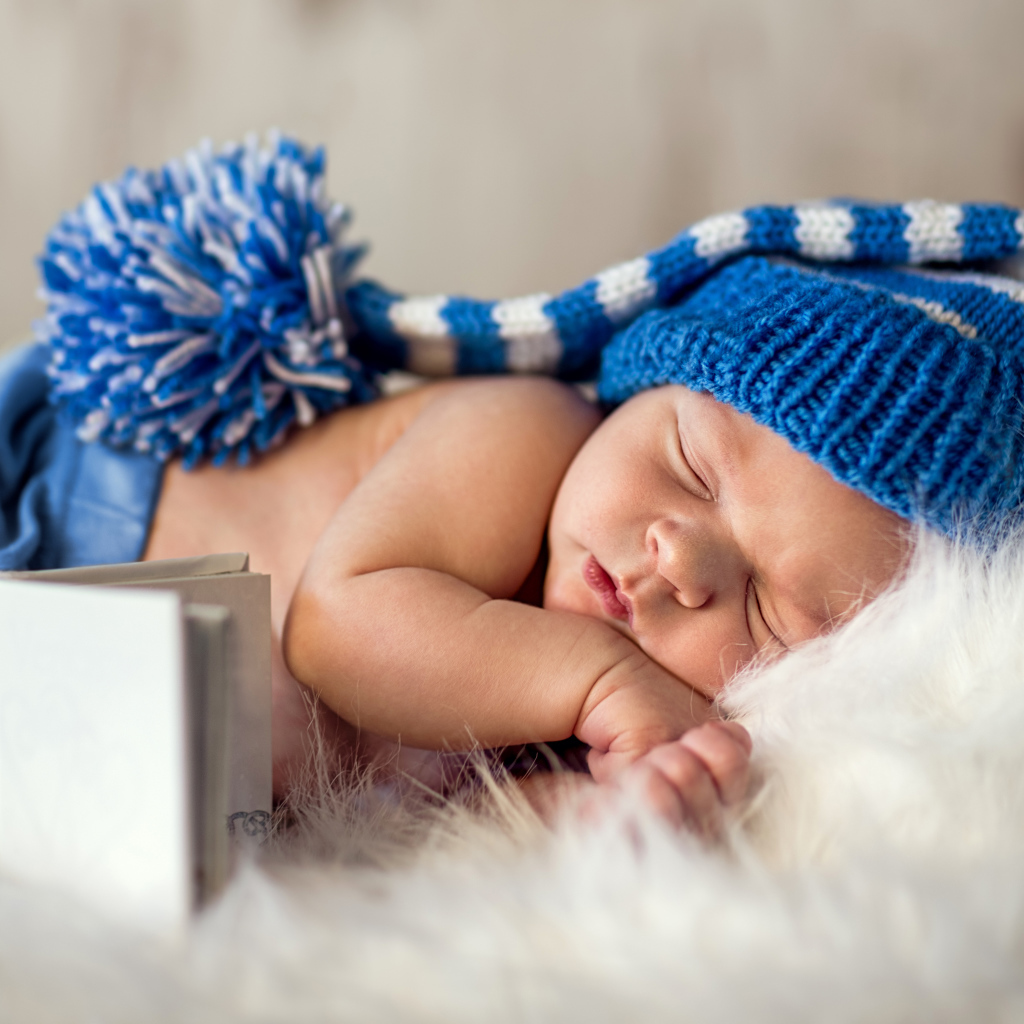 Маленький спящий грудной ребенок в синей вязанной шапке 