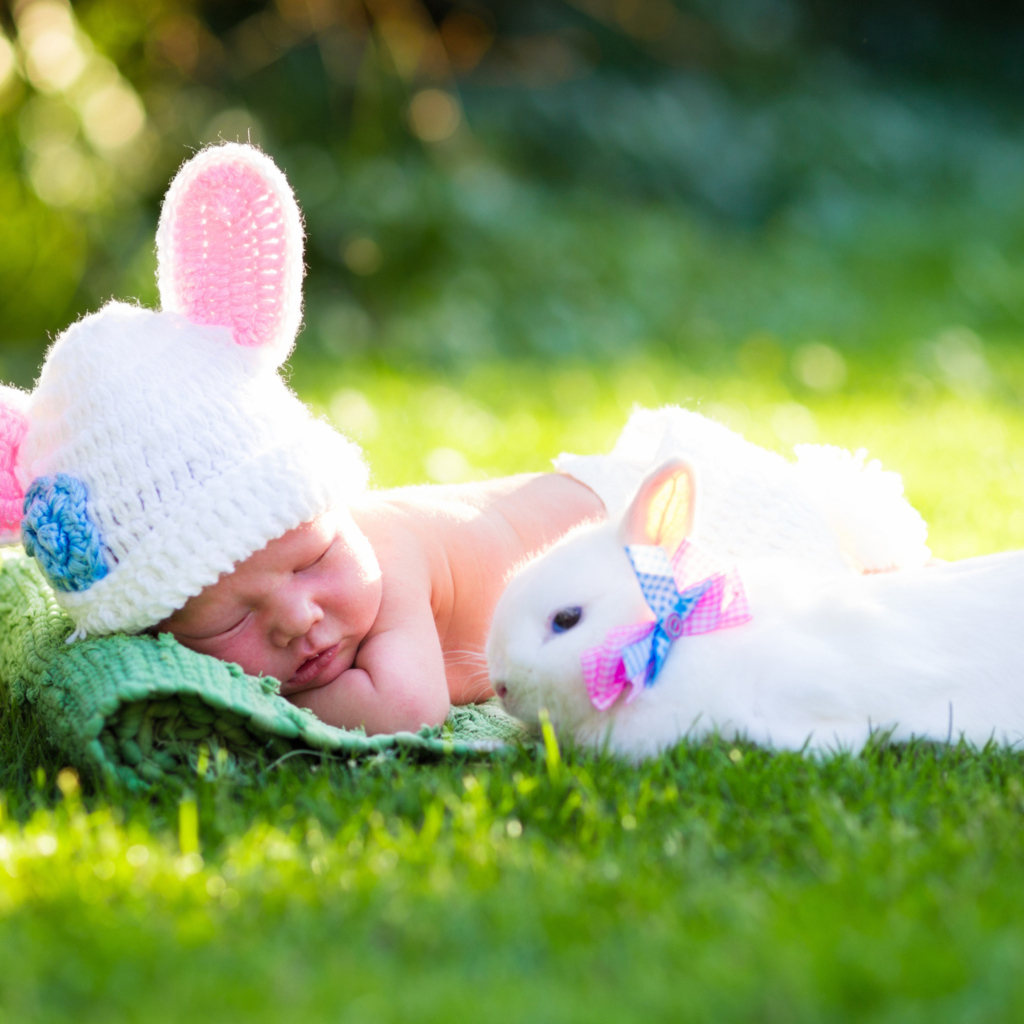 Маленький спящий грудной ребенок на зеленой траве с белым кроликом