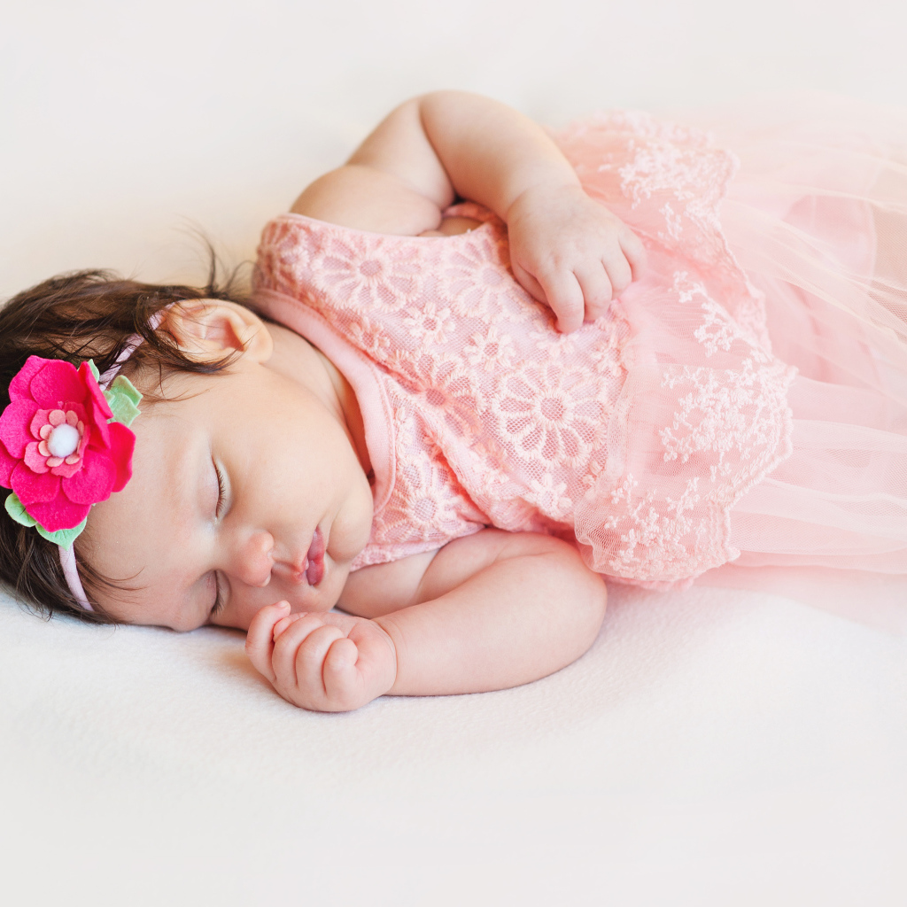 Маленькая спящая девочка в розовом платье с цветком в волосах 