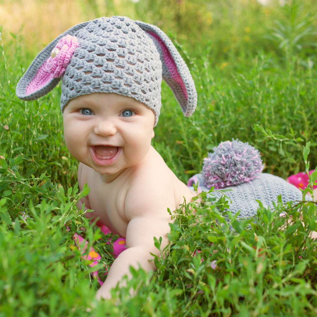 Маленький улыбающийся ребенок в костюме зайчика лежит в зеленой траве