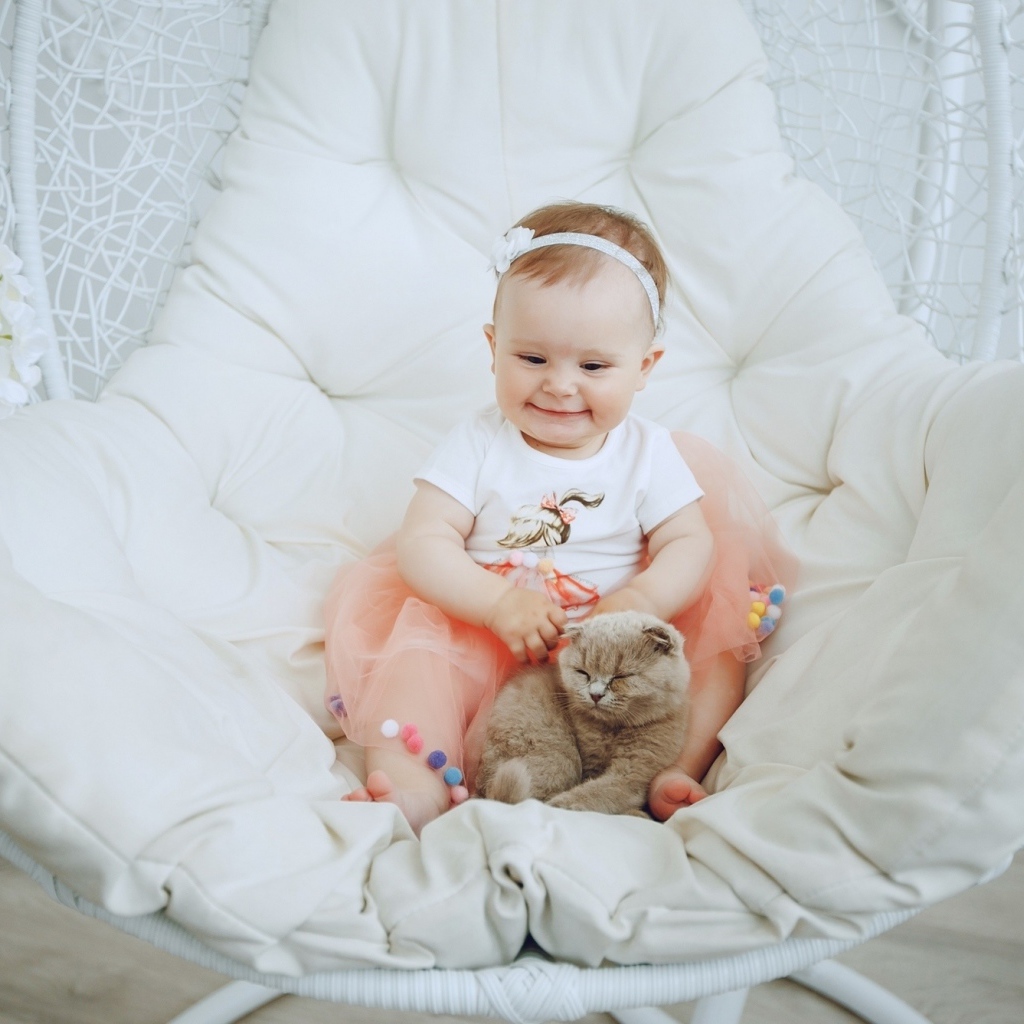 Маленький улыбающийся ребенок с котом сидит в белом кресле