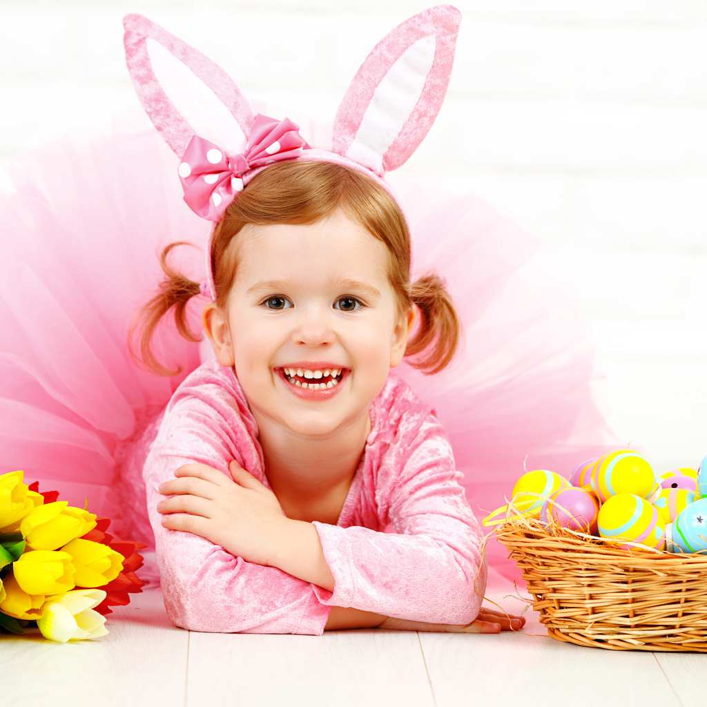 Маленькая улыбающаяся девочка в розовом с пасхальными яйцами и букетом тюльпанов