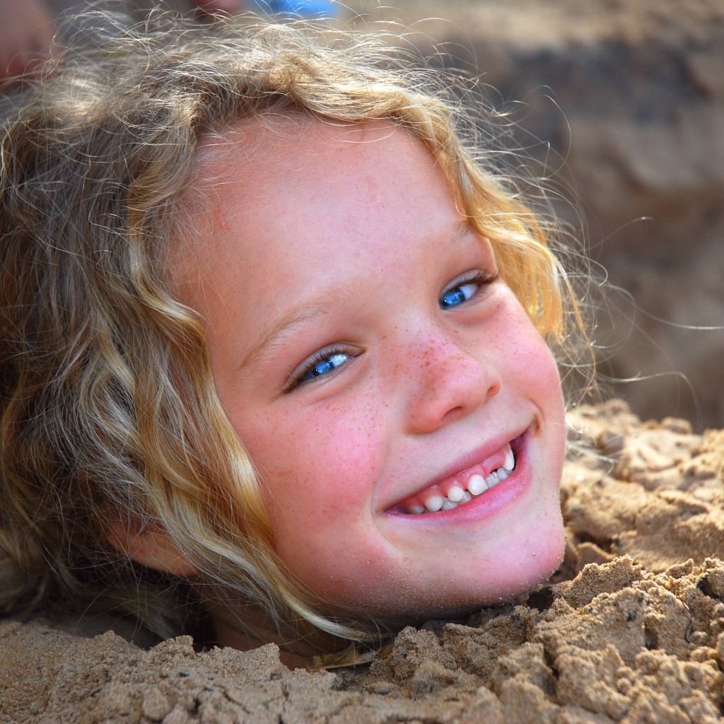 Маленькая улыбающаяся девочка играет в песке