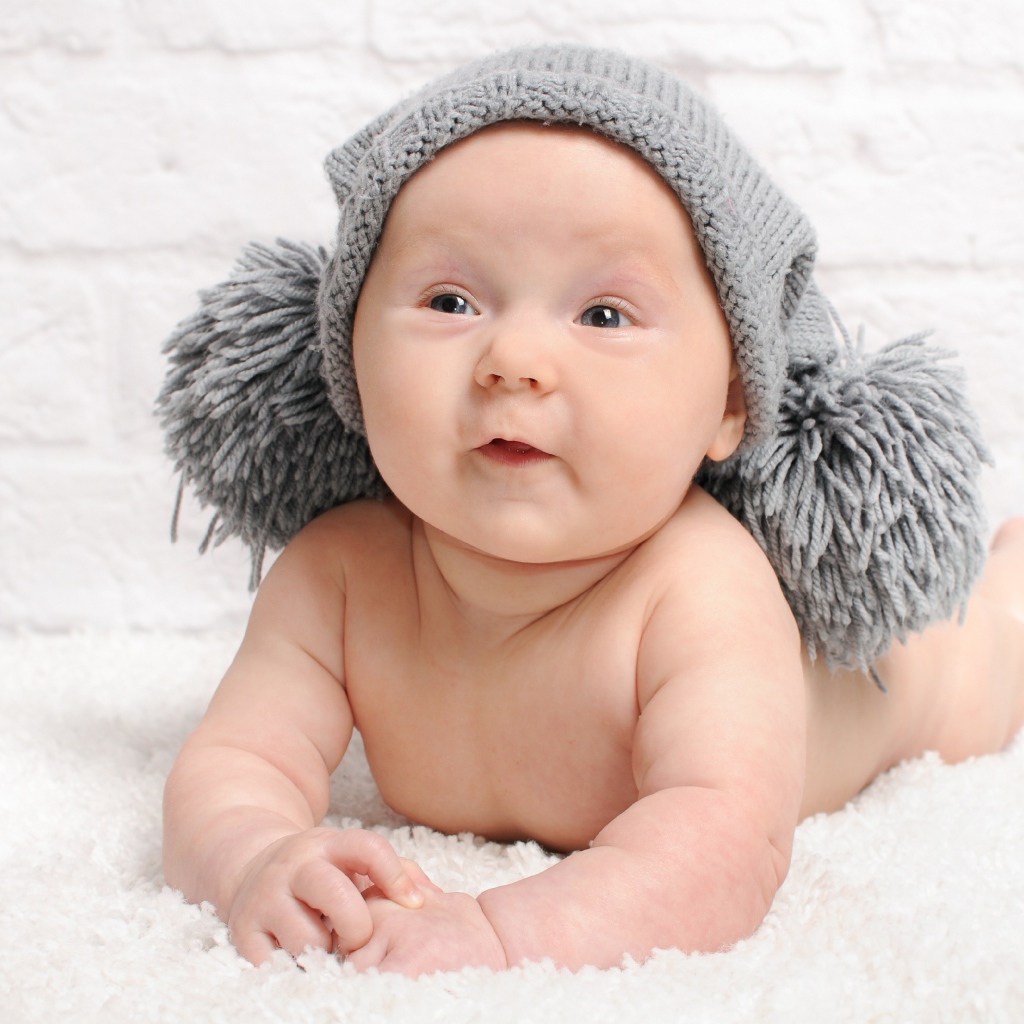 Улыбающийся грудной ребенок в серой шапке с бубонами