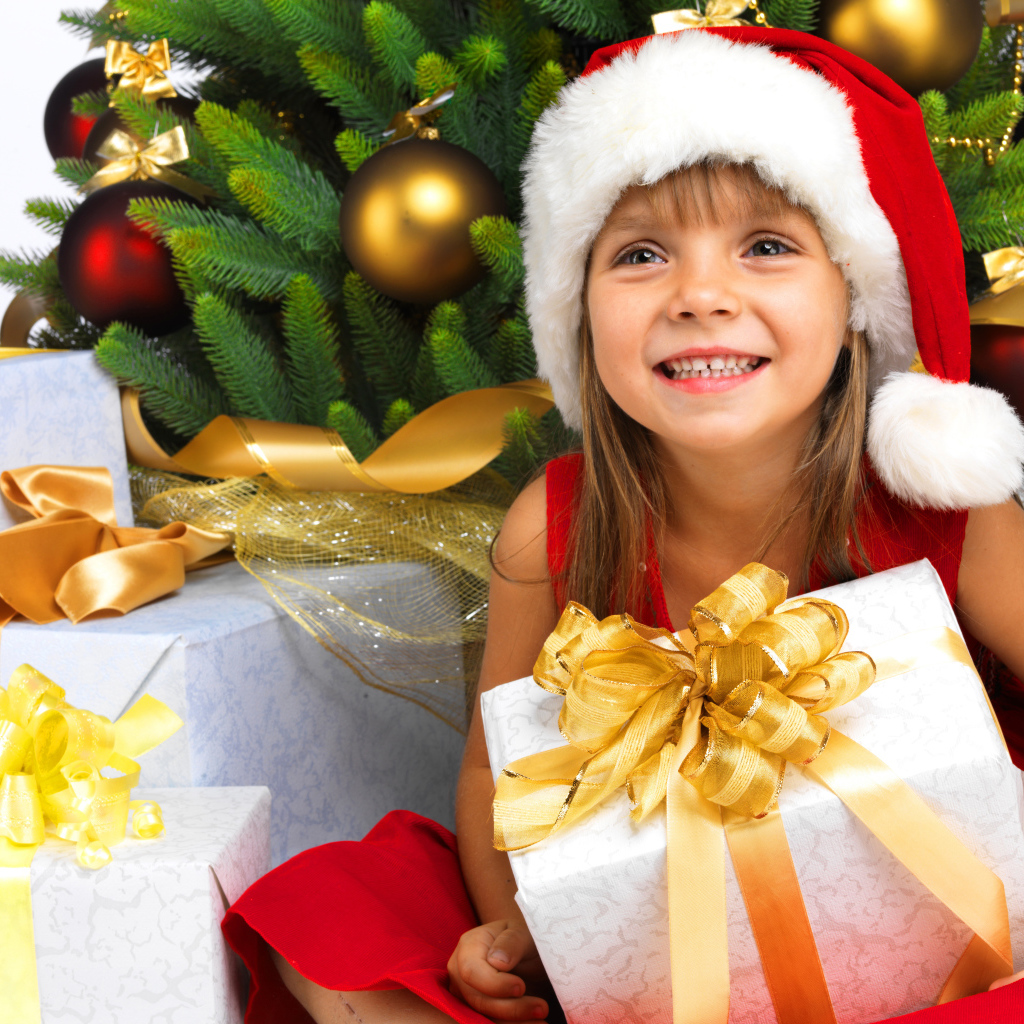 Улыбающаяся девочка в новогоднем костюме с подарками под елкой