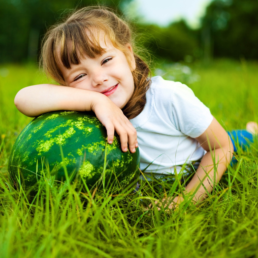 Улыбающаяся девочка с зеленым арбузом на траве