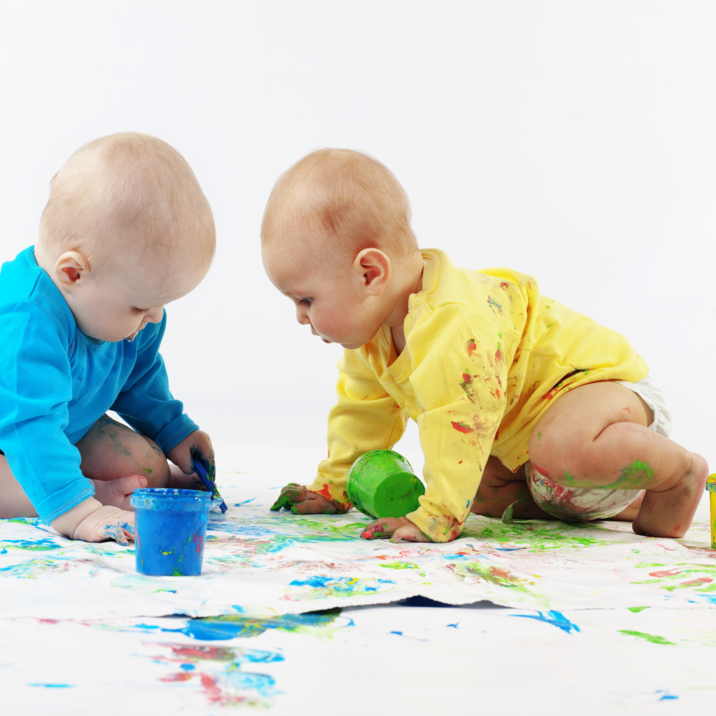 Два малыша рисуют красками на белом фоне