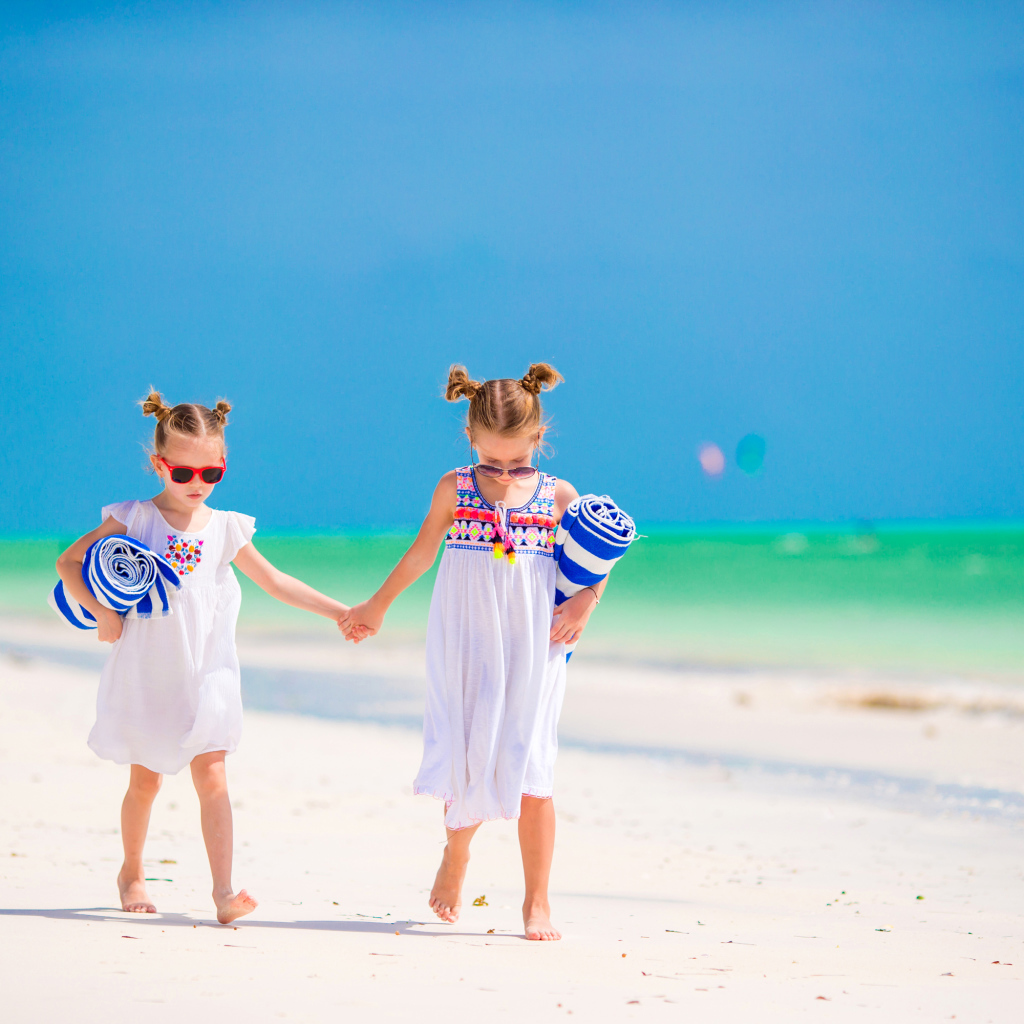 Две маленькие девочки идут по песку