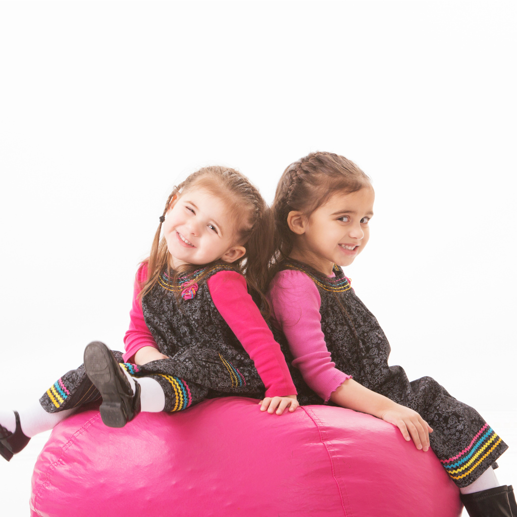 Две маленькие девочки сидят на красном мягком шаре 