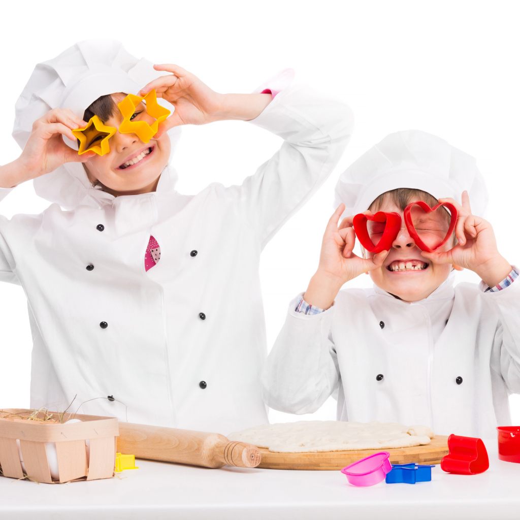 Два маленьких ребенка в костюмах повара готовят на кухне печенье