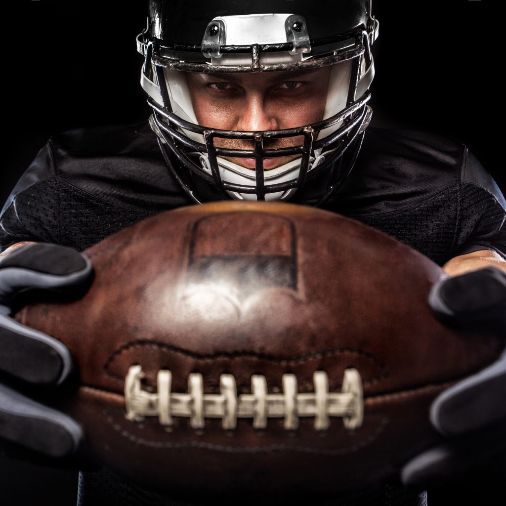 Американский футболист с мячом на черном фоне
