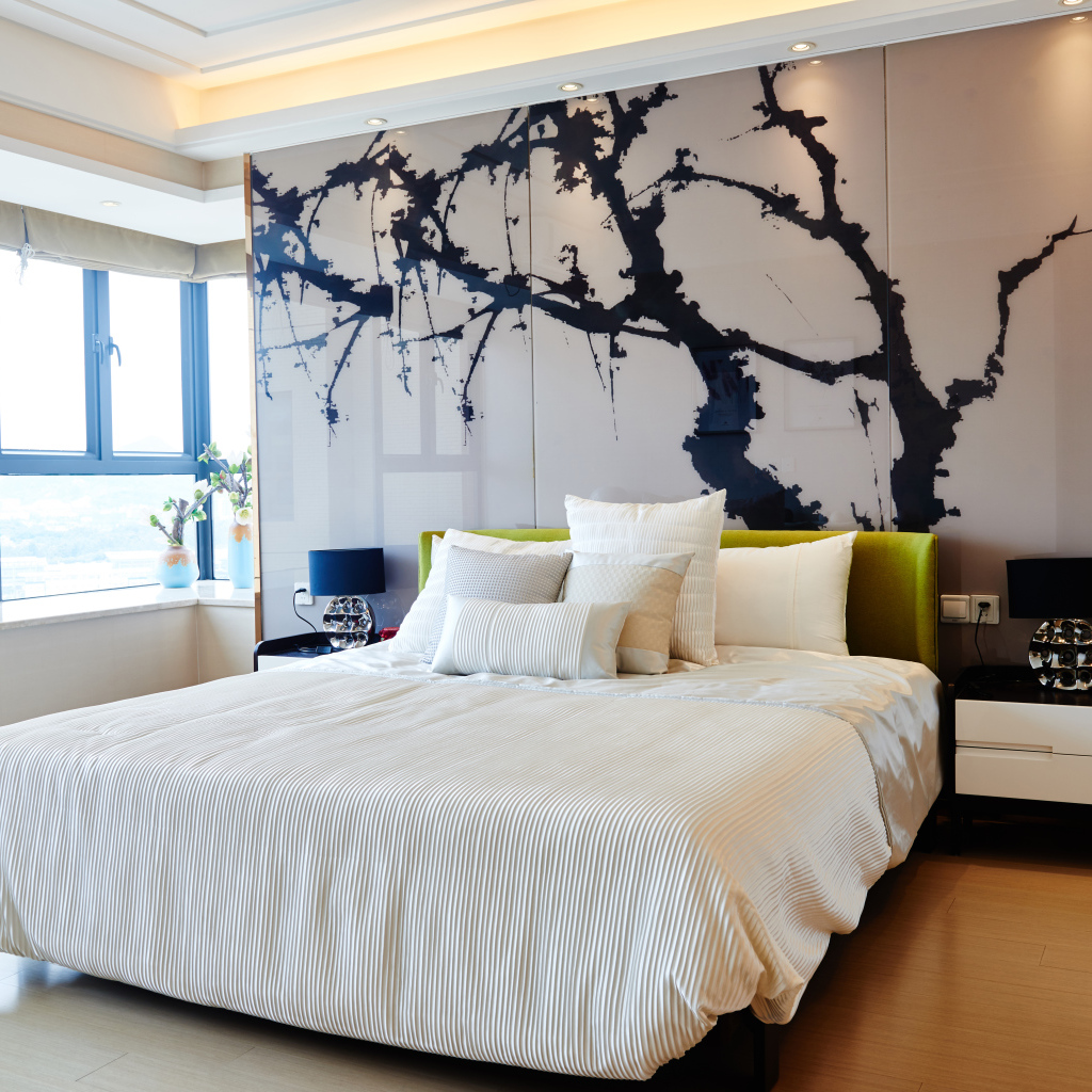 Красивая светлая спальня с большой кроватью и рисунком на стене 