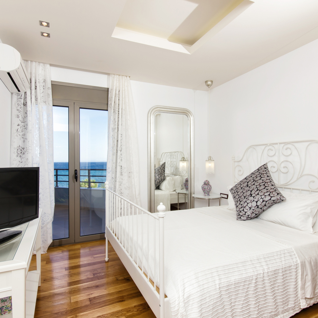 Светлая спальня с большой белой кроватью и телевизором 