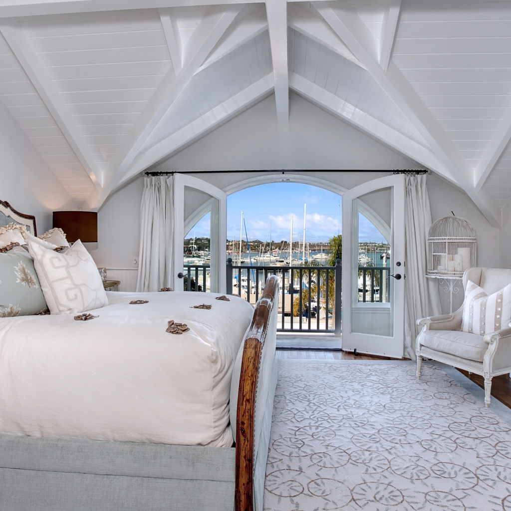 Белая спальня с большой высокой кроватью и балконом 