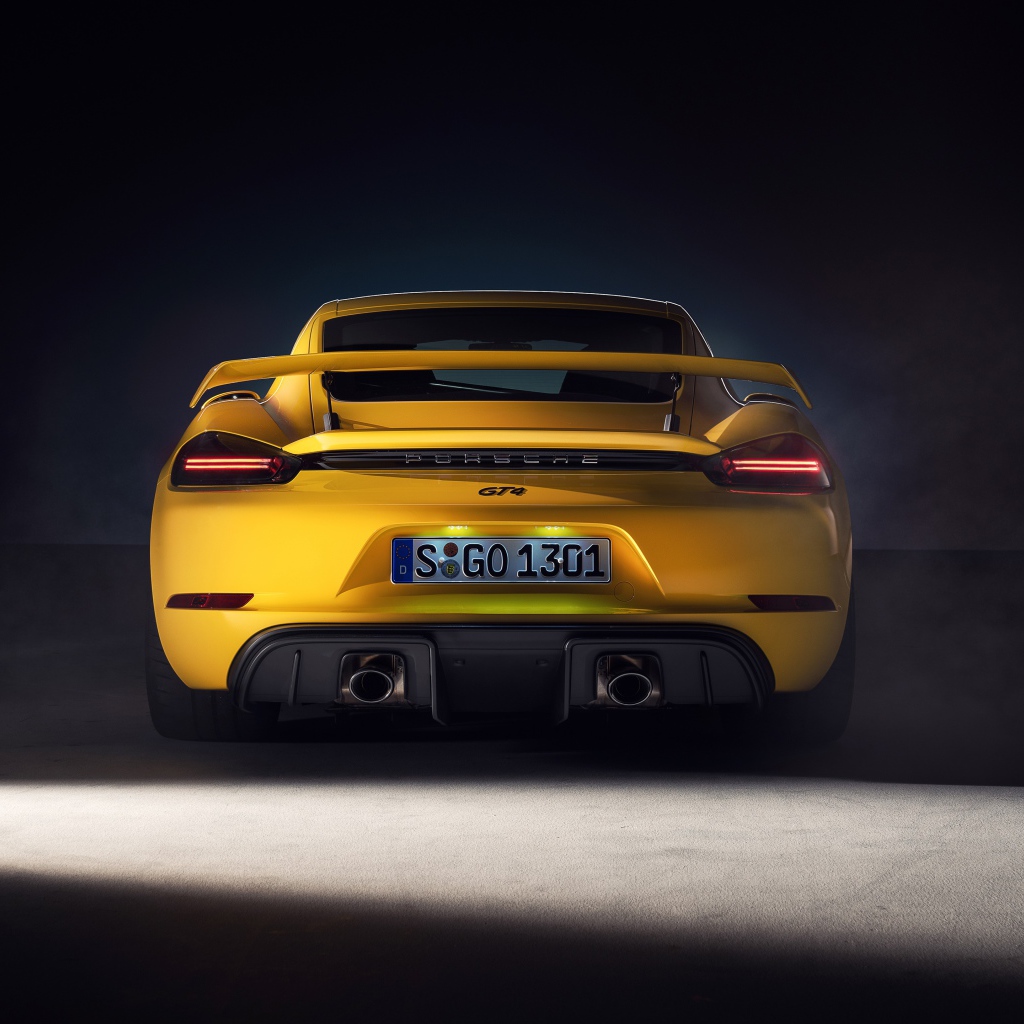 Желтый автомобиль Porsche 718 Cayman GT4, 2019 года вид сзади на сером фоне