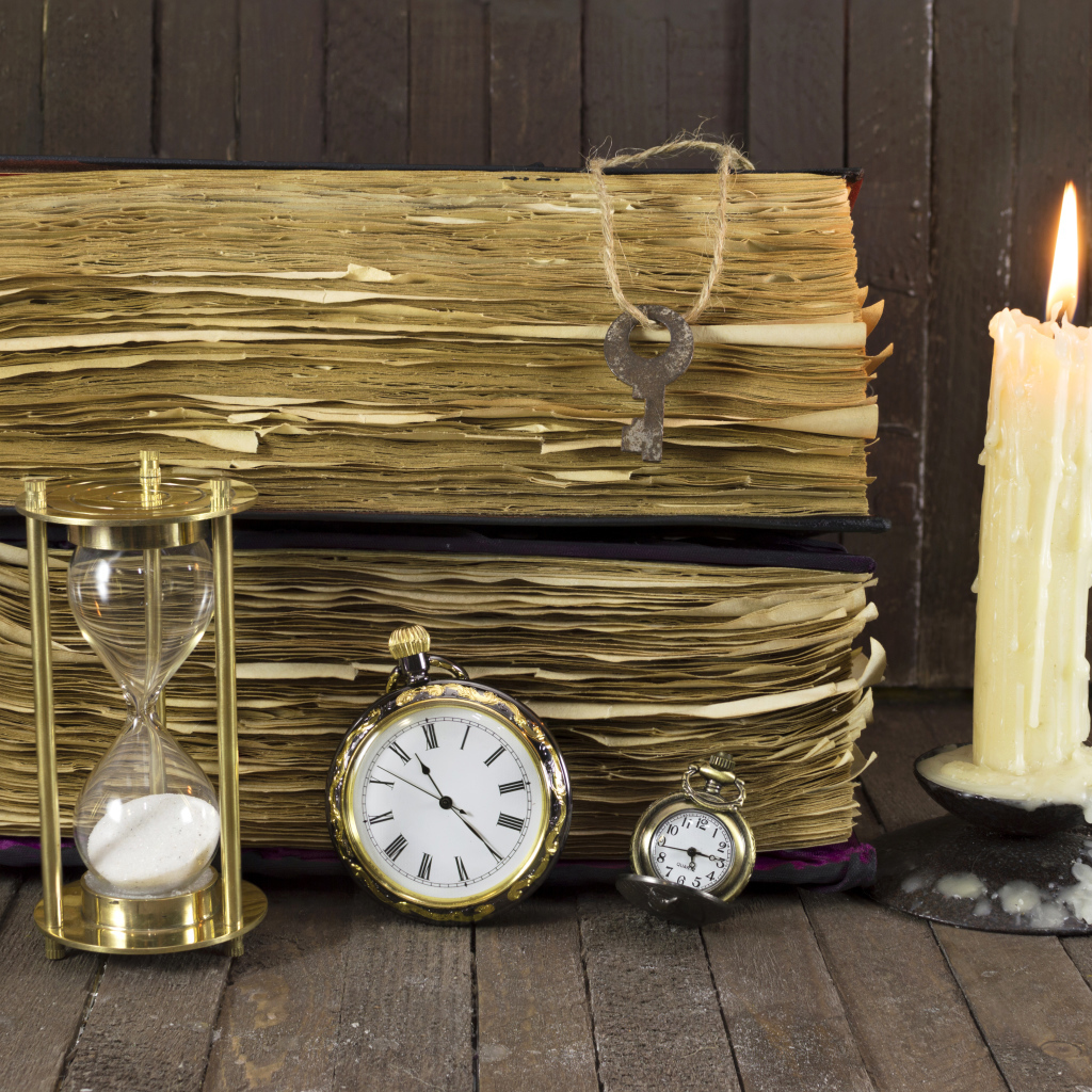 Старинные книги, зажженная свеча, ключи и часы на столе