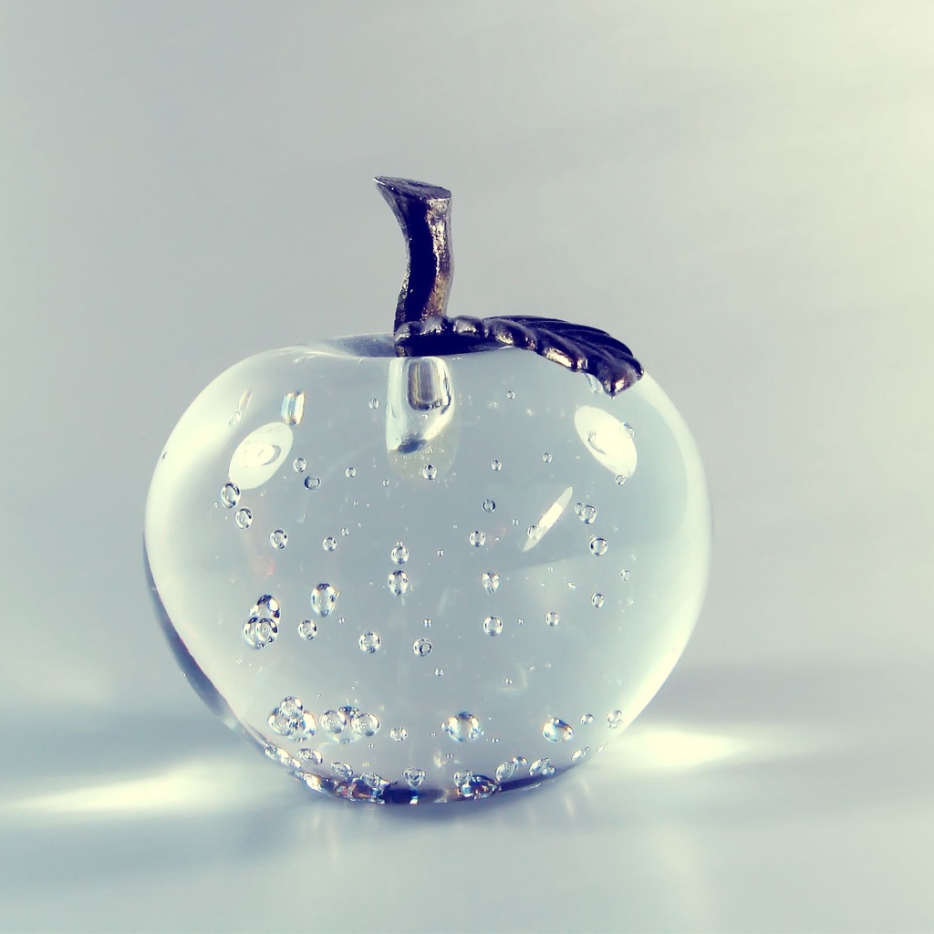 Стеклянное яблоко на сером фоне 