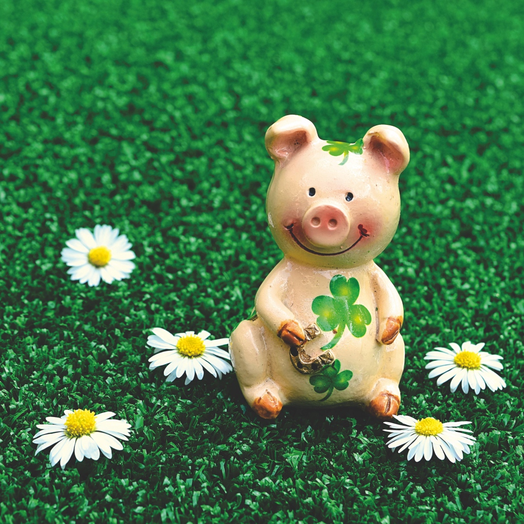 Статуэтка поросенка на зеленой траве с ромашками