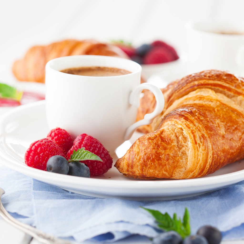 Чашка кофе на тарелке с круассаном и ягодами