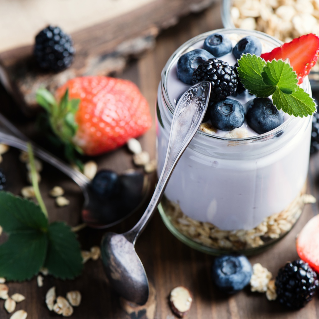 Баночка с мюсли, йогуртом и ягодами на столе с ложками