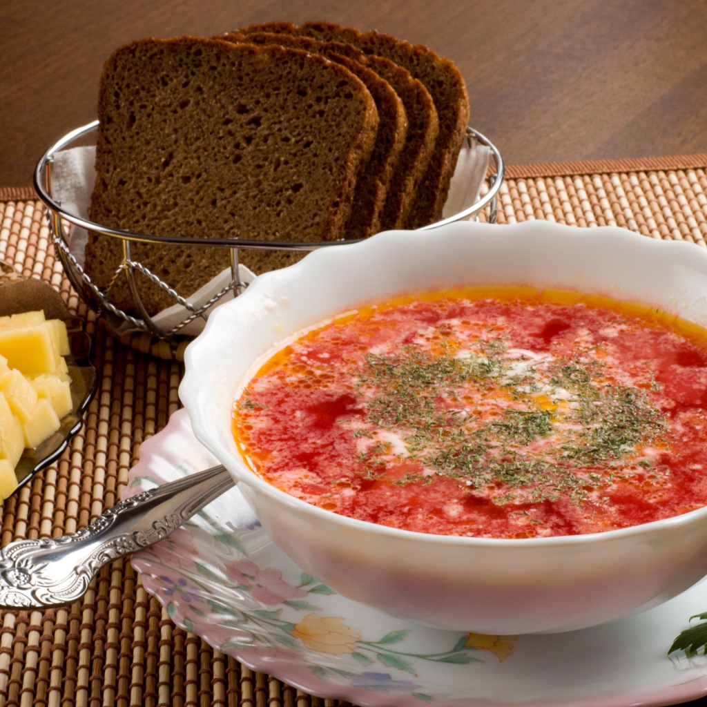 Тарелка красного борща на столе с сыром и черным хлебом