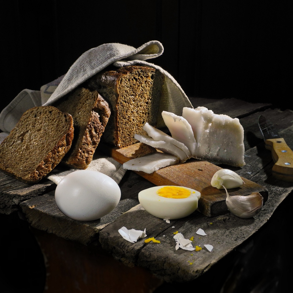Черный хлеб, вареные яйца, чеснок и сало на деревянном столе