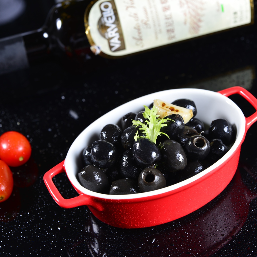 Черные оливки на столе с бутылкой и помидорами