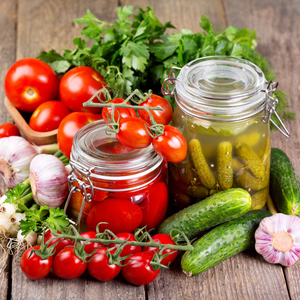 Консервированные помидоры и огурцы на столе со свежими овощами и зеленью 