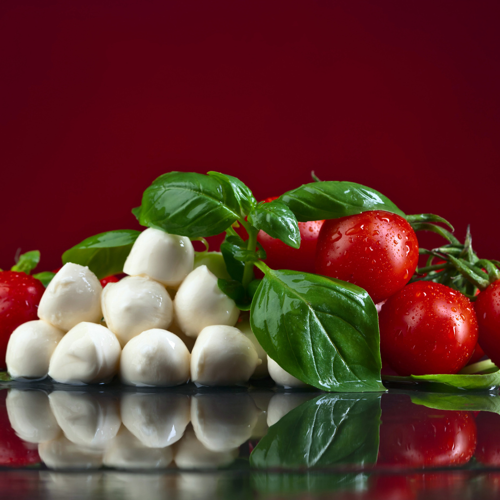 Сыр на столе с зеленью базилика и красными помидорами