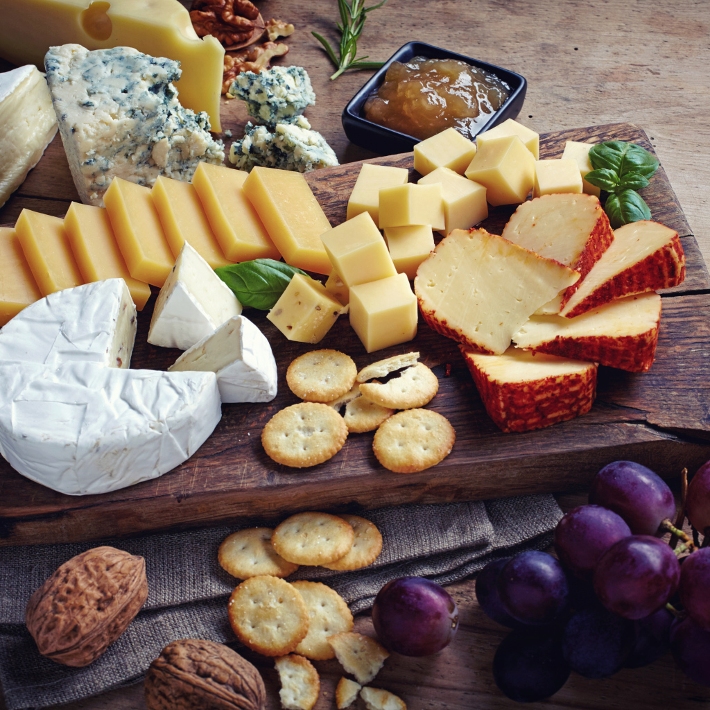 Сырная нарезка на разделочной доске на столе с виноградом и крекерами