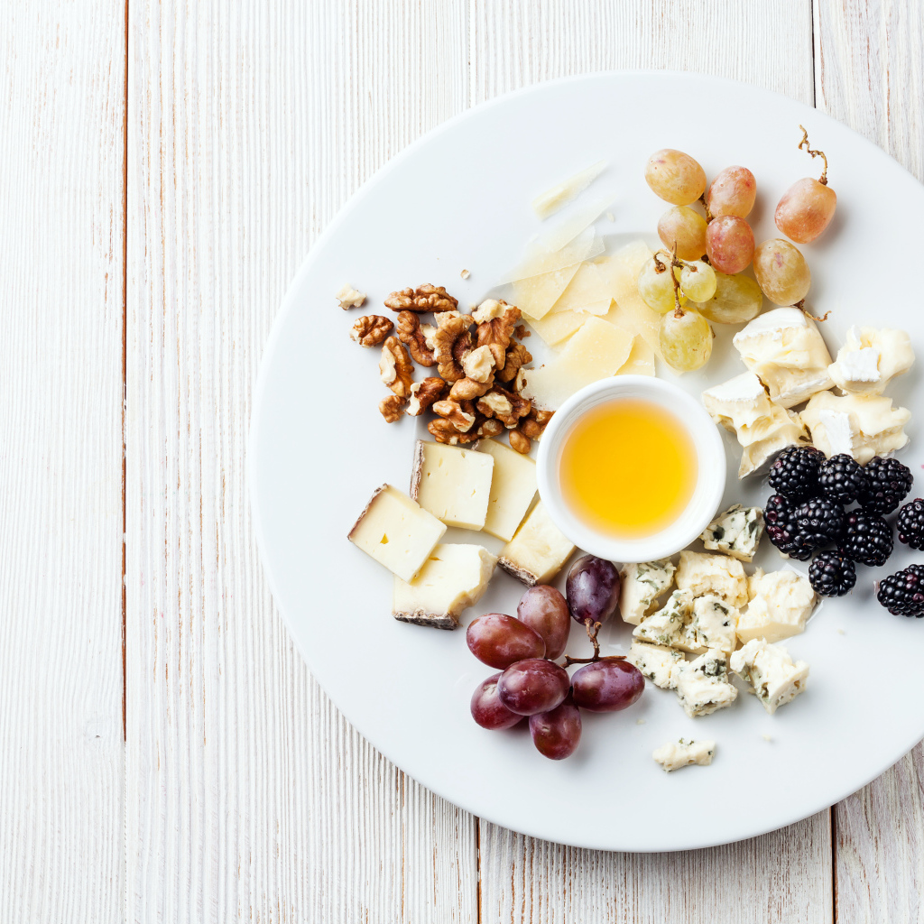 Куски сыра на тарелке с орехами, виноградом, медом и ягодами ежевики