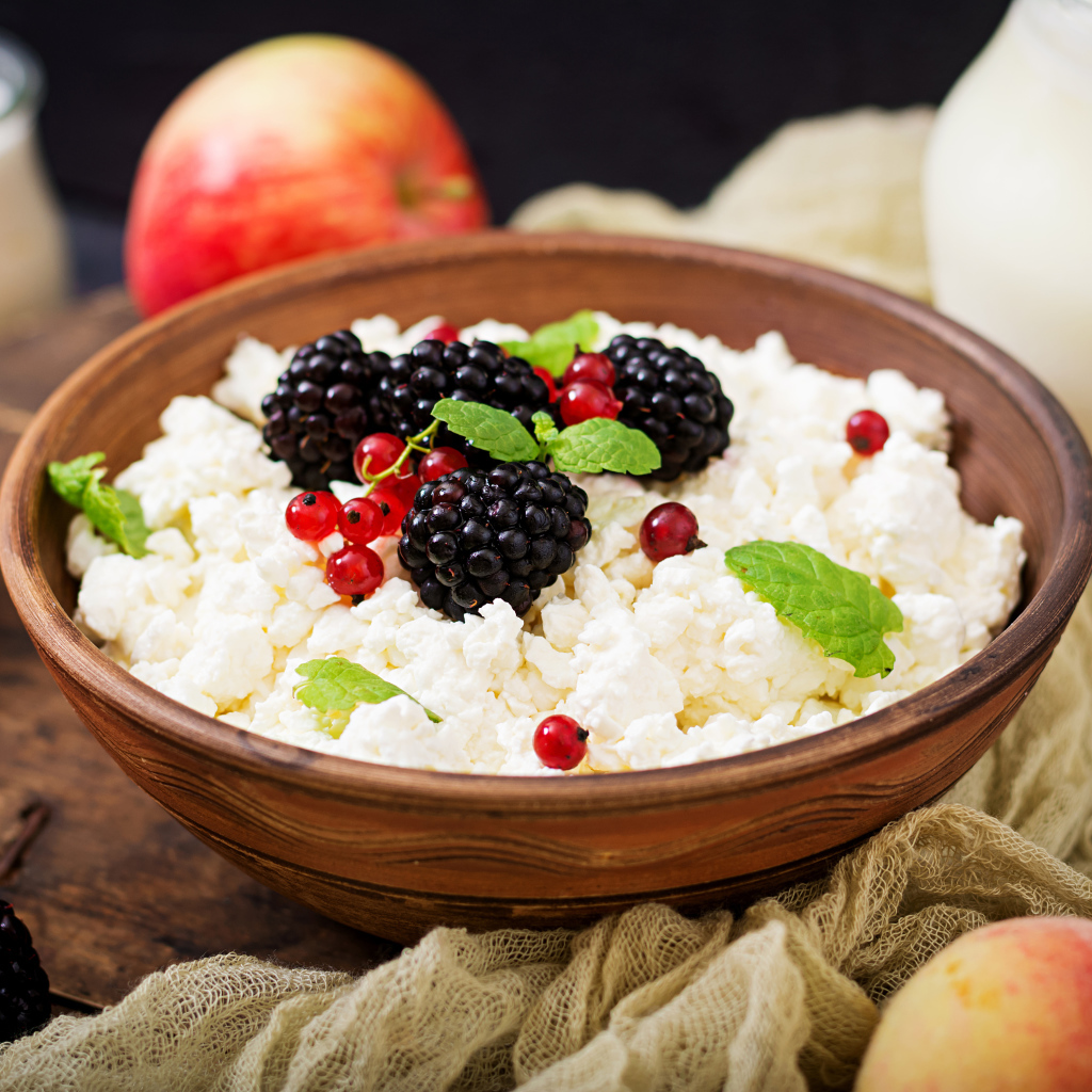 Творог с ягодами в деревянной миске на столе с яблоками