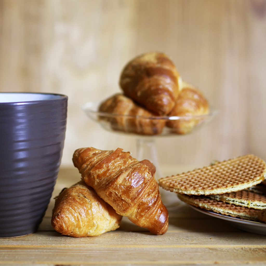 Чашка на столе с круассанами и вафлями 