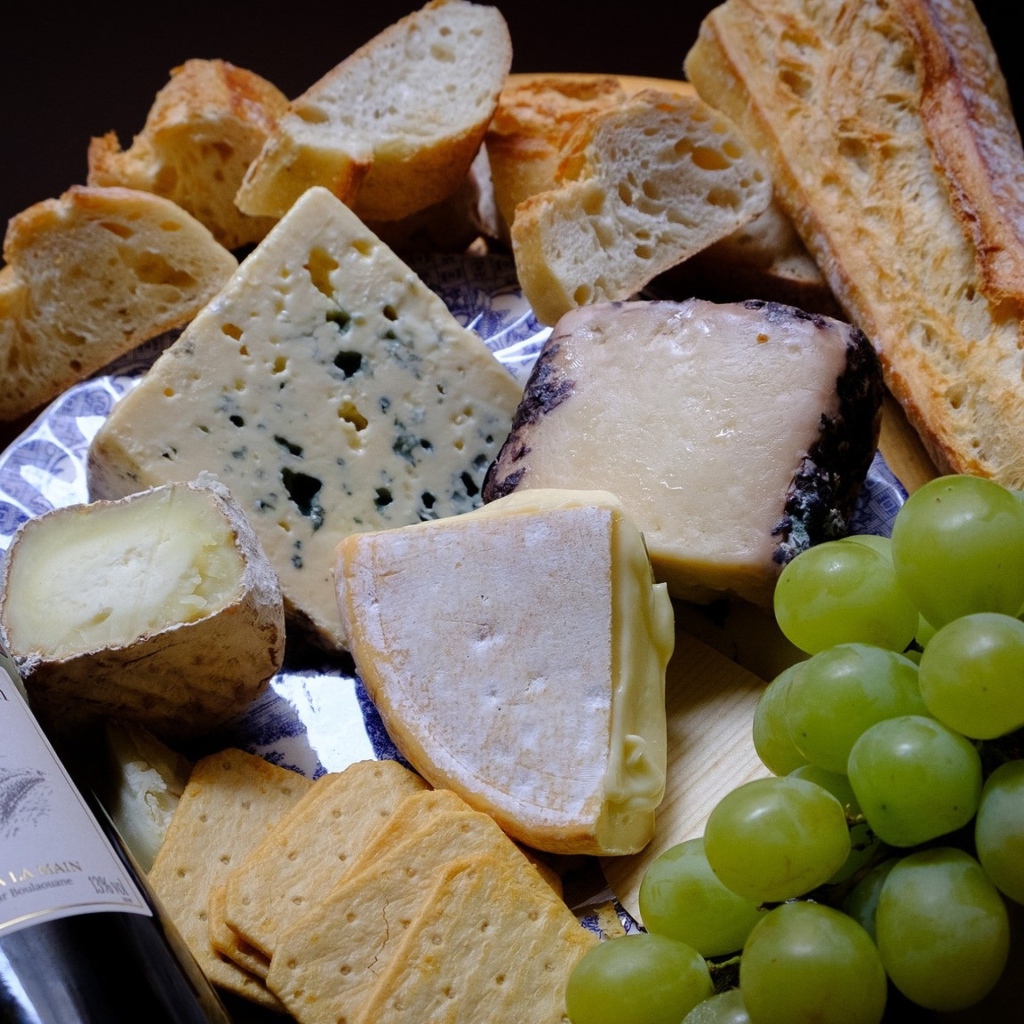 Разные виды твердого сыра на тарелке с белыми виноградом и вином